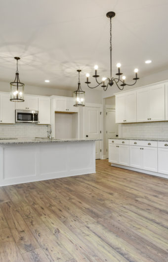 Newly built kitchen with white cabinets, an island, and wooden flooring.